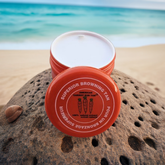 A container of Americas Carrot Sun Tan tanning cream with a red lid, featuring product information on the label.