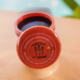 A container of Americas Carrot Sun Tan tanning cream with a red lid. Closed 